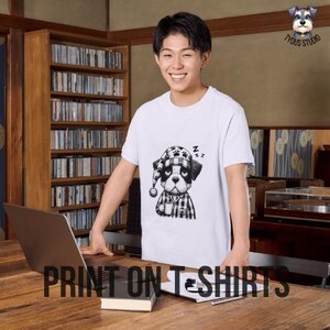 Pu&ograve; includere: Una maglietta bianca con un'illustrazione in bianco e nero di un cane che indossa un berretto da notte e tiene una tazza. Il cane indossa una camicia a quadri. Il testo "Zzz" &egrave; sopra la testa del cane. Il testo "PRINT ON T-SHIRTS" &egrave; nella parte inferiore dell'immagine.