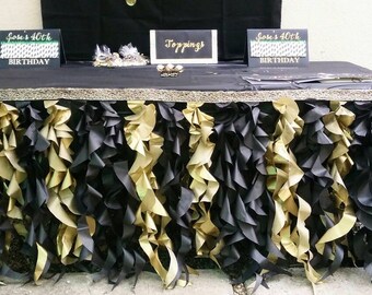 May include: A black table with a gold and black ruffled table skirt. There are three signs on the table, one that says "Joe's 40th Birthday", one that says "Joe's 40th Birthday", and one that says "Toppings".