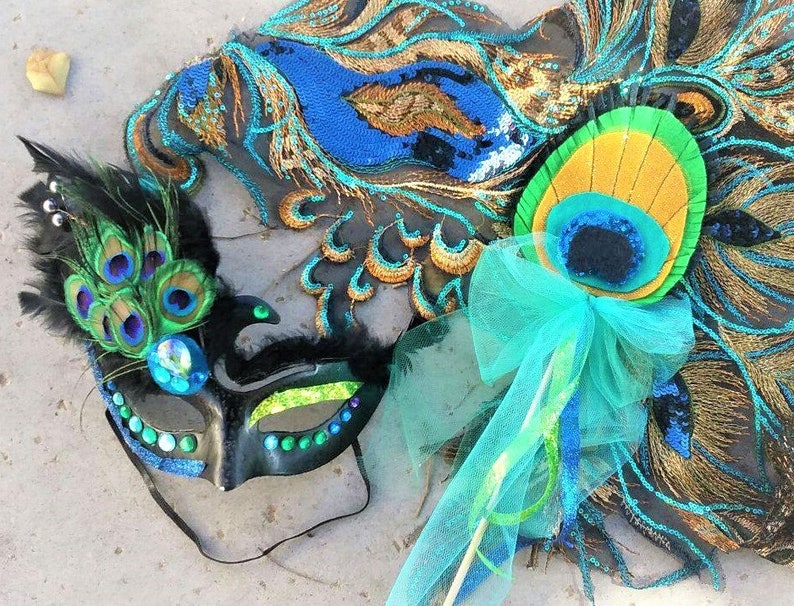 May include: A black masquerade mask with green and blue accents and peacock feathers. A peacock feather wand with a blue tulle bow.