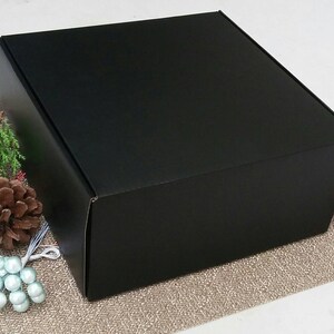 May include: A black cardboard box with a square shape. The box is sitting on a brown textured surface.