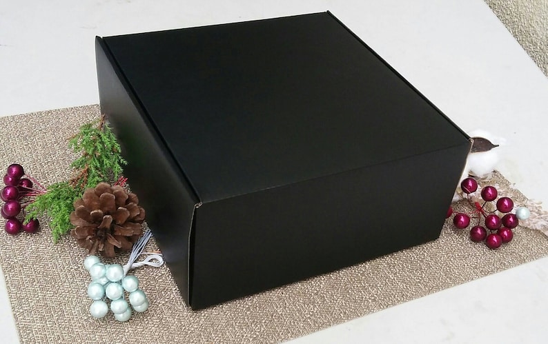 May include: A black cardboard box with a square shape. The box is sitting on a brown textured surface.