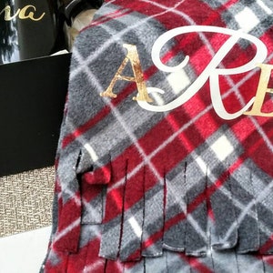 May include: A red and grey plaid fleece blanket with gold fringe and the monogram "A.R.B." embroidered in white.
