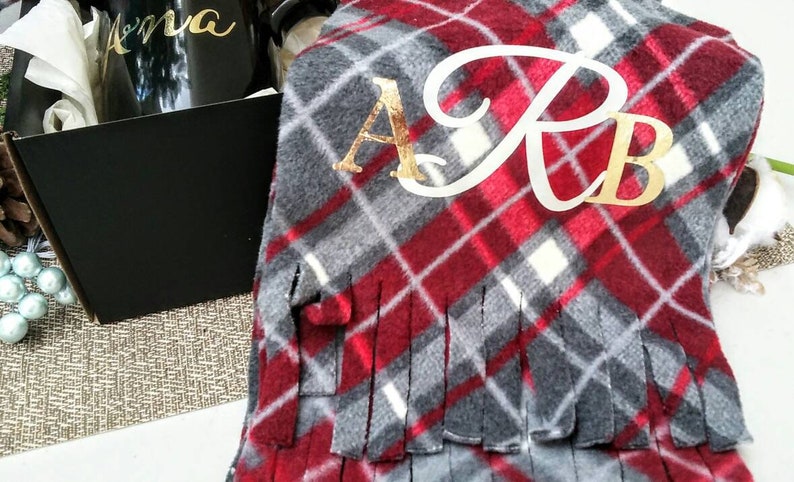 May include: A red and grey plaid fleece blanket with gold fringe and the monogram "A.R.B." embroidered in white.
