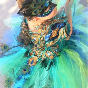 May include: A girl wearing a peacock-themed costume with a blue and green tulle skirt, gold and blue sequined bodice, and a peacock feather mask.