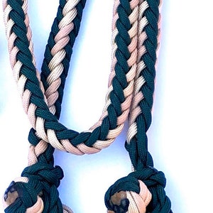 May include: A braided rope with two knots at the ends. The rope is made of two colours: dark green and light beige.