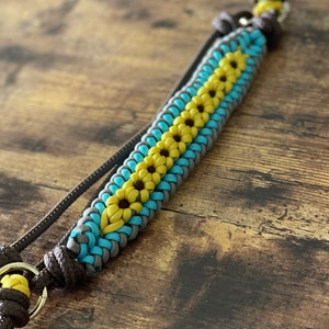 Pu&ograve; includere: Una corda intrecciata marrone, blu e gialla con un anello di metallo dorato a un'estremit&agrave;. La corda &egrave; intrecciata in un motivo che ricorda i fiori.