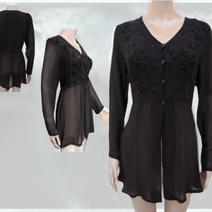 Op de afbeelding: Een zwarte, doorschijnende blouse met lange mouwen, een V-hals en een knoopsluiting aan de voorkant. De blouse is versierd met zwarte kralen in een bloemenpatroon.