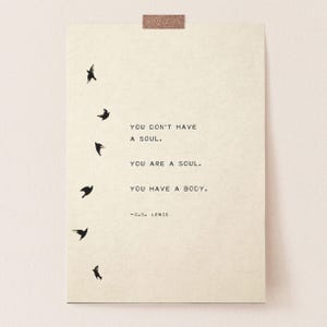 May include: A rectangular off-white paper print featuring six small black bird silhouettes flying in a vertical column on the left side. The text reads: YOU DON'T HAVE A SOUL. YOU ARE A SOUL. YOU HAVE A BODY. -C.S. LEWIS. A small piece of tape is at the top.