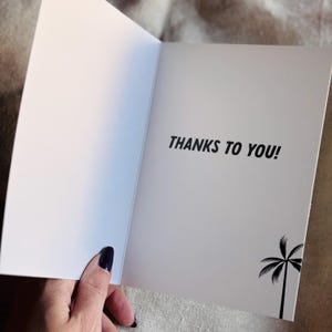 Pu&ograve; includere: Un biglietto d'auguri vuoto con una silhouette di palma e il testo "THANKS TO YOU!" stampato sul davanti.