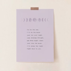 May include: A lavender print featuring a series of moon phases at the top and a poem below. The poem reads, "You be the sun. I'll be the moon- just let your light come shining through; and when night comes, just like the moon, I'll shine the light right back to you."