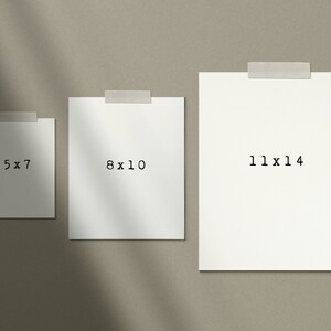 K&ouml;nnte beinhalten: Drei wei&szlig;e rechteckige Papierst&uuml;cke, die an eine beige Wand geklebt sind. Das Papier ist leer, au&szlig;er dem Text "5 x 7", "8 x 10" und "11 x 14", der in Schwarz gedruckt ist.