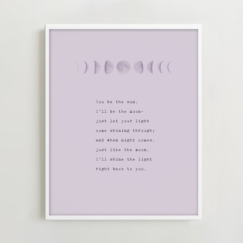 May include: A framed print featuring a light purple background with a series of moon phase illustrations. The print includes the text "You be the sun, I'll be the moon..." in a typewriter font, creating a celestial theme.