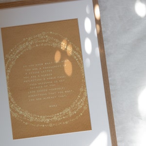 May include: A framed print with a gold background and white text. The text reads: "DO YOU KNOW WHAT YOU ARE? YOU ARE A MANUSCRIPT OF A DIVINE LETTER YOU ARE A MIRROR REFLECTING A NOBLE FACE. THIS UNIVERSE IS NOT OUTSIDE OF YOU. LOOK INSIDE YOURSELF: EVERYTHING THAT YOU WANT, YOU ARE ALREADY THAT. RUMI"