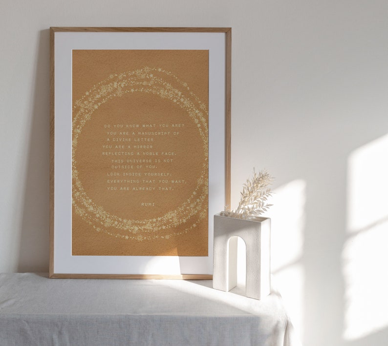 May include: A framed print with a beige background and gold glitter stars forming a circle around a quote by Rumi. The quote reads: "Do you know what you are? You are a manuscript of a divine letter. You are a mirror reflecting a noble face. This universe is not outside of you. Look inside yourself. Everything that you want, you are already that."