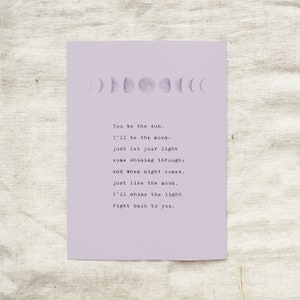 May include: A lavender print featuring a moon phase illustration and a poem. The poem reads, "You be the sun. I'll be the moon- just let your light come shining through; and when night comes, just like the moon, I'll shine the light right back to you."
