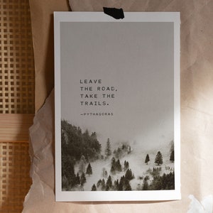 May include: A black and white print with a quote by Pythagoras: "Leave the road, take the trails." The print features a misty forest scene with trees and fog.