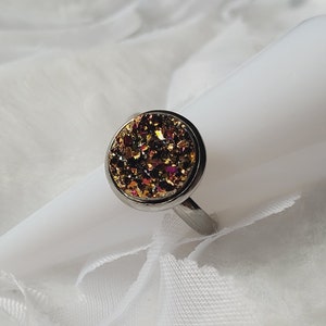 May include: A silver ring featuring a round, sparkly, iridescent gemstone in shades of gold, orange, and red.
