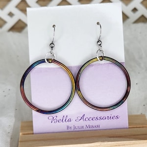 May include: A pair of rainbow coloured hoop earrings with silver hooks. The earrings are on a display stand with a purple background and the text "Bella Accessories by Julie Misasi".