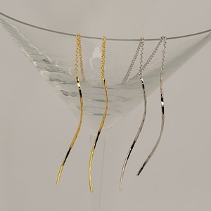 Op de afbeelding: Drie paar lange, dunne, hangende oorbellen. De oorbellen zijn gemaakt van een dunne, gedraaide ketting. Een paar is goud, een paar is zilver en een paar is een mix van goud en zilver.