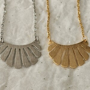 May include: Two delicate necklaces with a fan-shaped pendant. One necklace is silver and the other is gold.