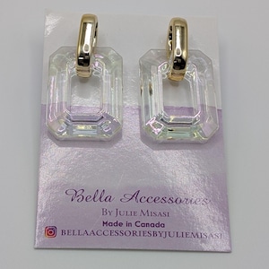 Może przedstawiać: Para kolczyków z przezroczystych, tęczowych kryształów z złotymi obręczami. Kolczyki są prezentowane na kartce z tekstem "Bella Accessories By Julie Misasi Made in Canada Bellaaccessoriesbyjuliemisasi".