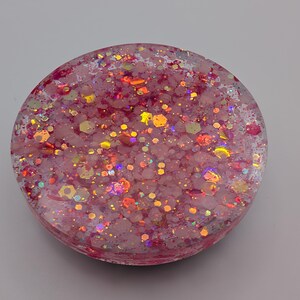 May include: A circular resin coaster featuring a translucent pink base embedded with a dense mixture of multi-sized hexagonal and fine glitter particles in shades of pink, gold, and iridescent orange that reflect light across the surface.
