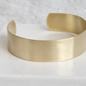 May include: A simple, brushed gold cuff bracelet. The bracelet is made from a single piece of metal and has a smooth, rounded finish.
