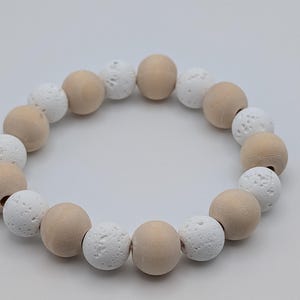 May include: A circular bracelet made of alternating light brown wooden beads and white, textured beads. The beads are approximately 2 cm in diameter. The bracelet is strung on an elastic cord. The colour palette is neutral.