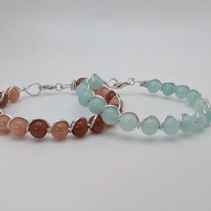 May include: Two wire-wrapped bracelets with light blue and peach colored beads.