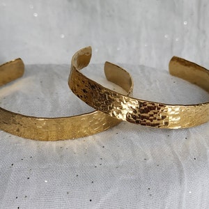 Peut inclure: Deux bracelets en métal martelé de couleur dorée. Les bracelets sont empilés l'un sur l'autre.