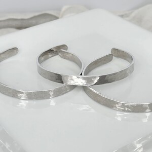 Peut inclure: Trois bracelets en métal argenté martelé empilés sur une surface blanche.