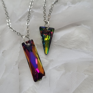 Puede incluir: Dos collares con colgantes de cristal iridiscente. Un colgante es rectangular, el otro es triangular. Ambos colgantes tienen una gama de colores que incluyen púrpura, amarillo y verde. Las cadenas son de color plateado y están sobre un fondo blanco texturizado.