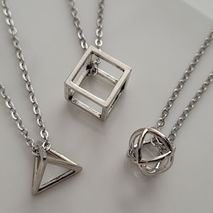 May include: Three silver necklaces with geometric pendant charms. The charms are a cube, a sphere, and a triangle.