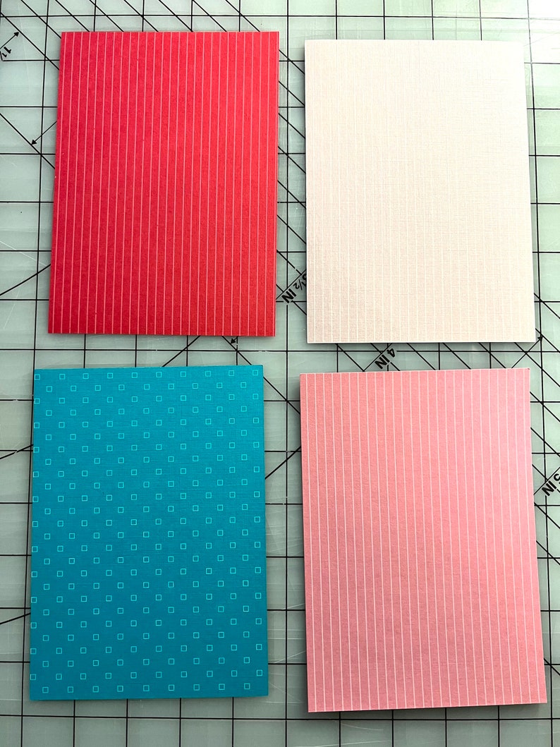 May include: Four rectangular patterned paper sheets. One is red with vertical white stripes, another is white with a subtle grid pattern, a third is teal with small white squares, and the last is pink with vertical white stripes.