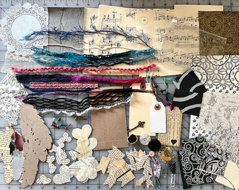 May include: A collection of craft supplies for scrapbooking and mixed media art. The supplies include paper, lace, fabric, yarn, ribbon, buttons, and other embellishments. The items are arranged on a gridded cutting mat.