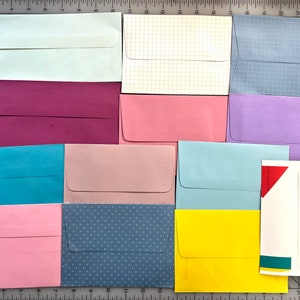 May include: Assortment of 12 envelopes in various colors and patterns, including plain, grid, polka dot, and solid colors. The envelopes are arranged in three rows of four.