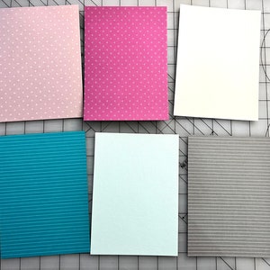 May include: Six rectangular cards with various patterns and colors. The cards include pink with white polka dots, magenta with small white triangles, and white. Additional cards feature teal with white stripes, light blue with vertical lines, and gray with white stripes.