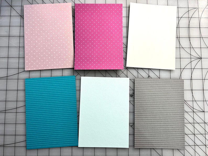 May include: Six rectangular cards with various patterns and colors. The cards include pink with white polka dots, magenta with small white triangles, and white. Additional cards feature teal with white stripes, light blue with vertical lines, and gray with white stripes.