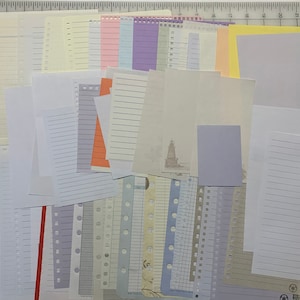 May include: A collection of assorted paper sheets in various colors and patterns, including lined, gridded, and blank paper. The papers are arranged in a random order and some have holes punched in the top.