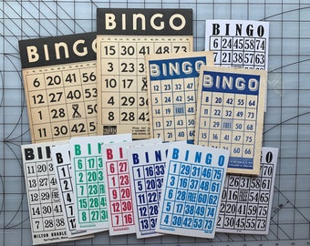 May include: A collection of vintage bingo cards with various designs and colors. The cards feature the word "BINGO" at the top, along with numbered squares. Some cards have blue, red, and green accents.