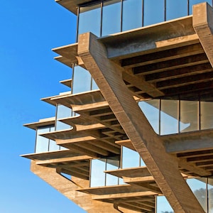 May include: A concrete building with a unique, layered design. The building features large windows and a series of cantilevered floors.