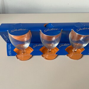 Può includere: Tre bicchieri da shot in vetro trasparente con basi arancioni, confezionati in una scatola blu con la scritta "Gille" stampata.