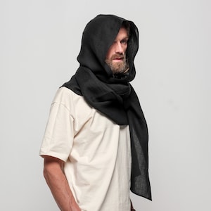 May include: A black hooded scarf made of linen. The scarf is worn by a person with a beard and is draped over the shoulders and head.