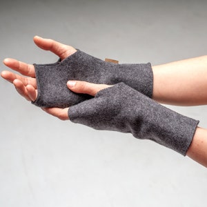 May include: A pair of grey fingerless gloves with a brown label. The gloves are made of a soft, warm material and are perfect for keeping your hands warm in the winter.