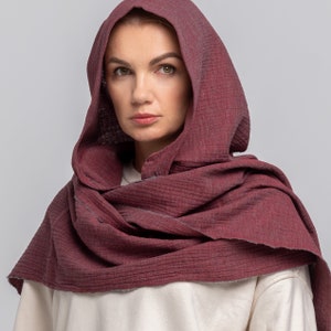 Pode incluir: Uma echarpe com capuz cor vinho feita de um tecido macio e texturizado. A echarpe está dobrada e drapeada sobre os ombros de uma pessoa.