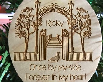 May include: A wooden ornament shaped like a rainbow bridge with a dog silhouette. The ornament is engraved with the text "Rainbow Bridge", "Ricky", "Once by my side... Forever in my heart", and "2007-2017".