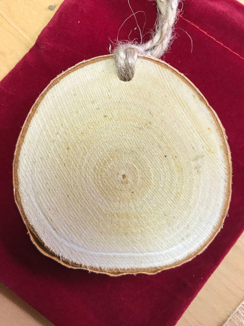May include: A round wooden ornament with a natural wood grain pattern and a hole in the top for hanging. The ornament is made from a slice of wood and has a rustic, natural look.