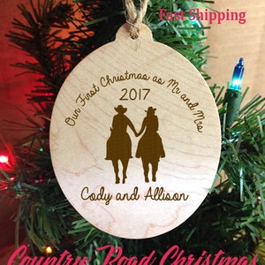 May include: A wooden Christmas ornament with the text "Our First Christmas as Mr and Mrs 2017" and "Cody and Allison". The ornament features a silhouette of a couple riding horses.