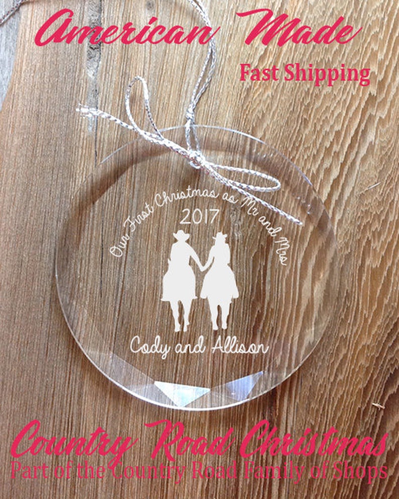 May include: Clear glass Christmas ornament with the text "Our First Christmas as Mr and Mrs 2017 Cody and Allison". The ornament features a silhouette of a couple in cowboy hats riding horses.