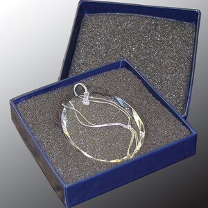 May include: A silver glass ornament with a swirling design is displayed in a blue velvet box with a black foam interior.